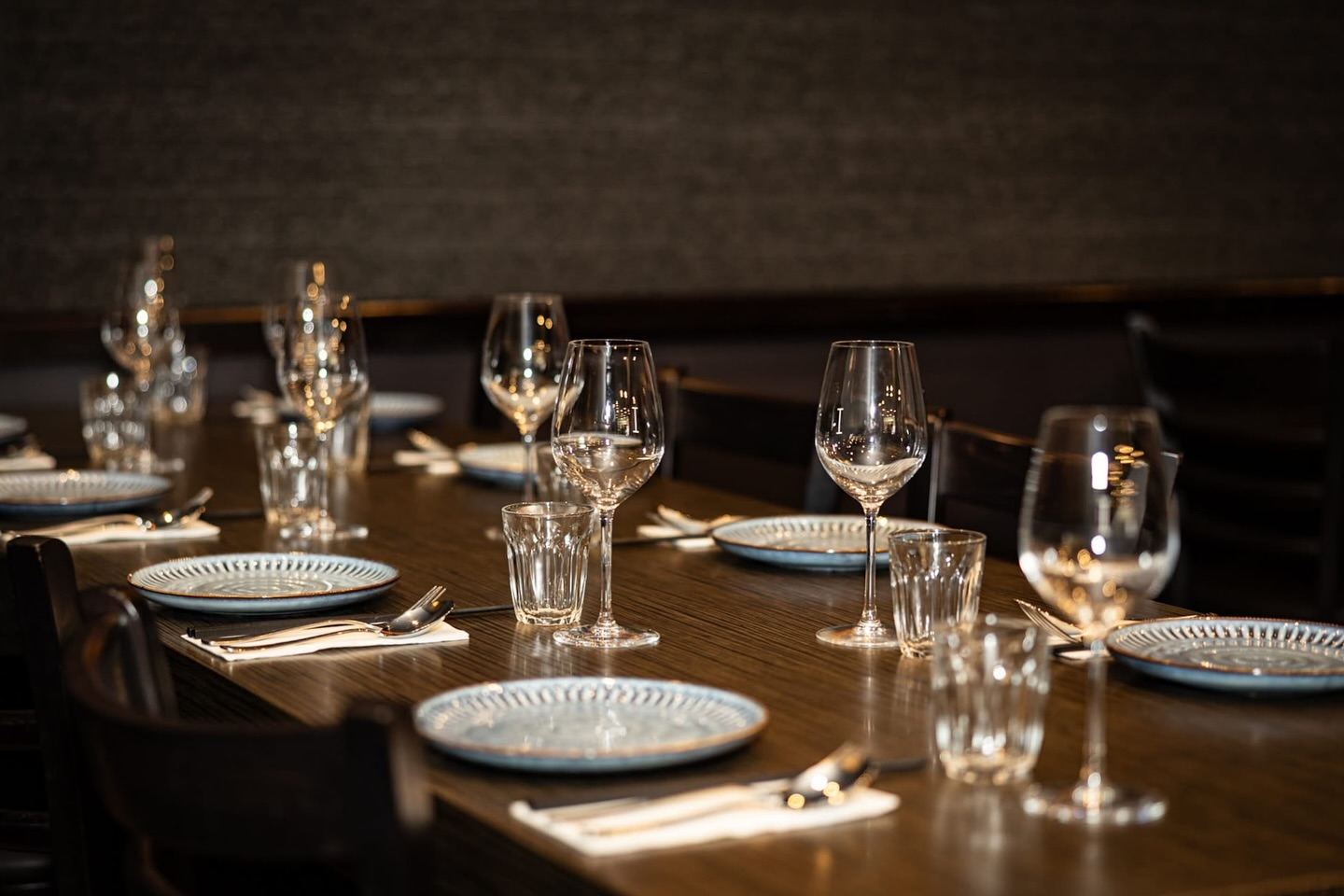 A long table set with wine glasses and blue ceramic plates in Ruby's dining room