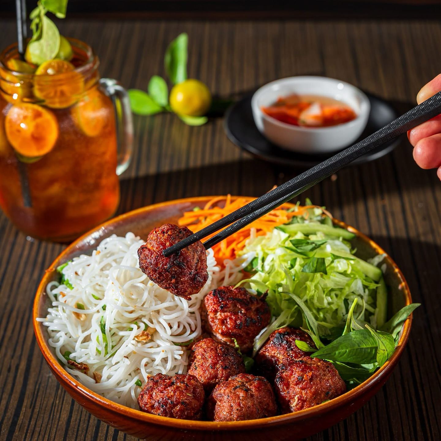 Vermicelli bowl with grilled pork balls, fresh herbs and an iced cumquat drink