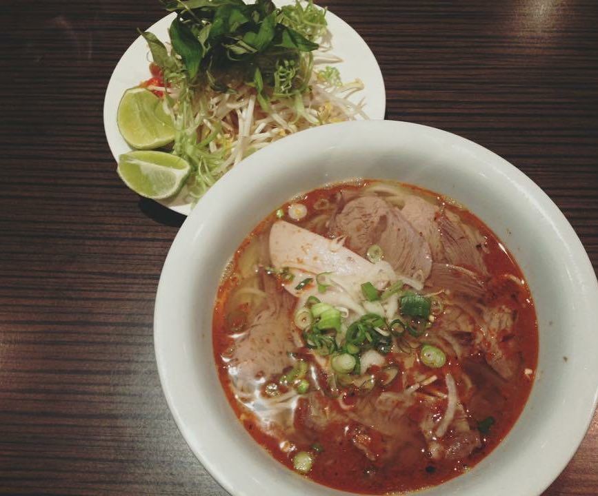 A bowl of bún bò Huế with herbs, bean sprouts and lime